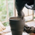 person in black gloves holding brown clay pot